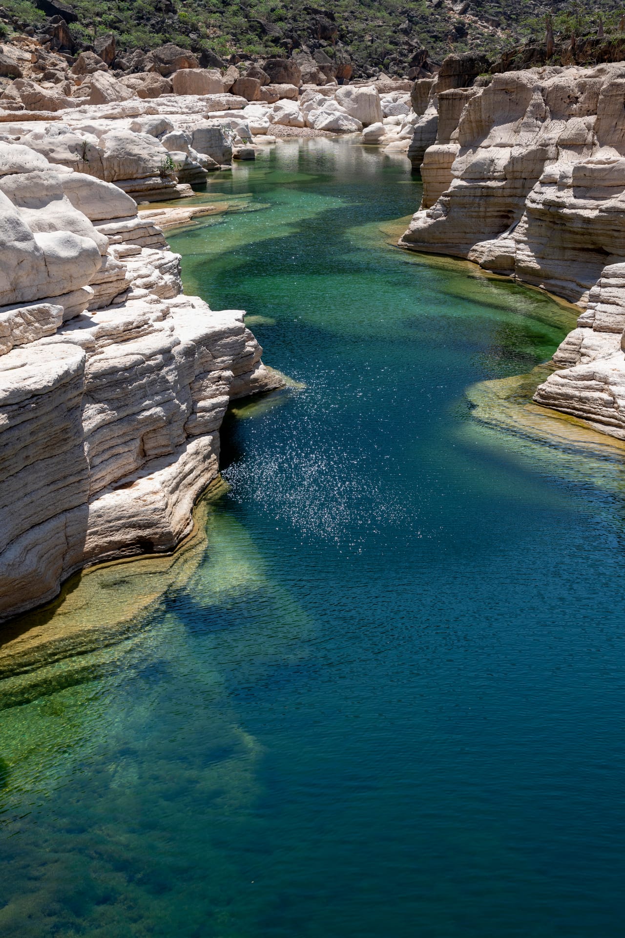 Green water running between layered white limestone walls in the Kalisan canyon.