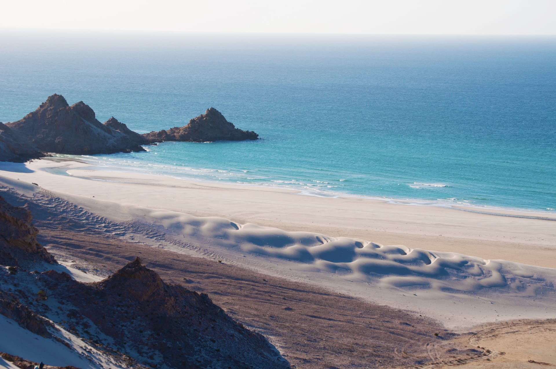 White sand dunes and a wide beach below dark rock headlands on the island’s western coast.