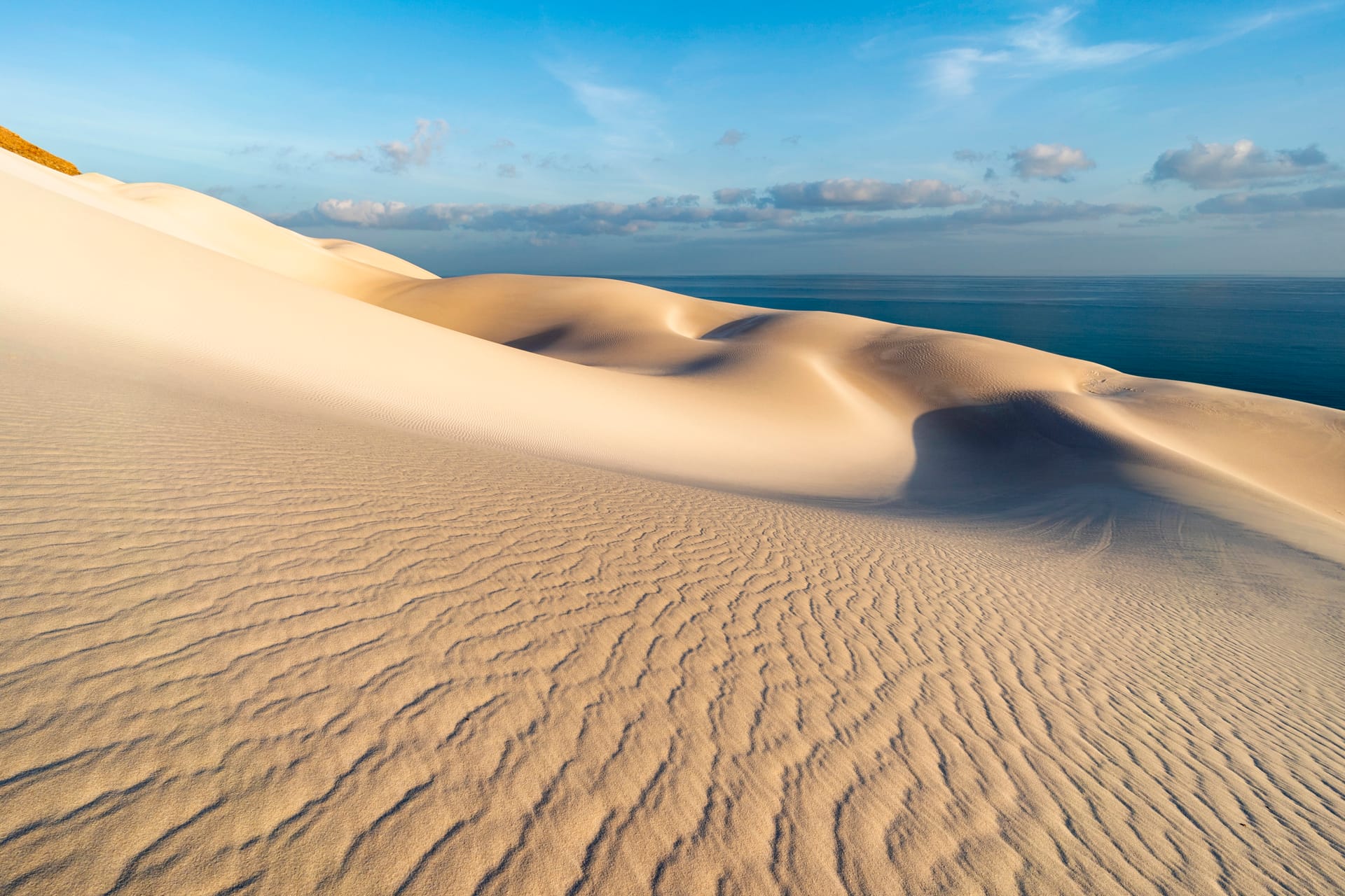 Wind-rippled white sand dunes running down towards the sea.