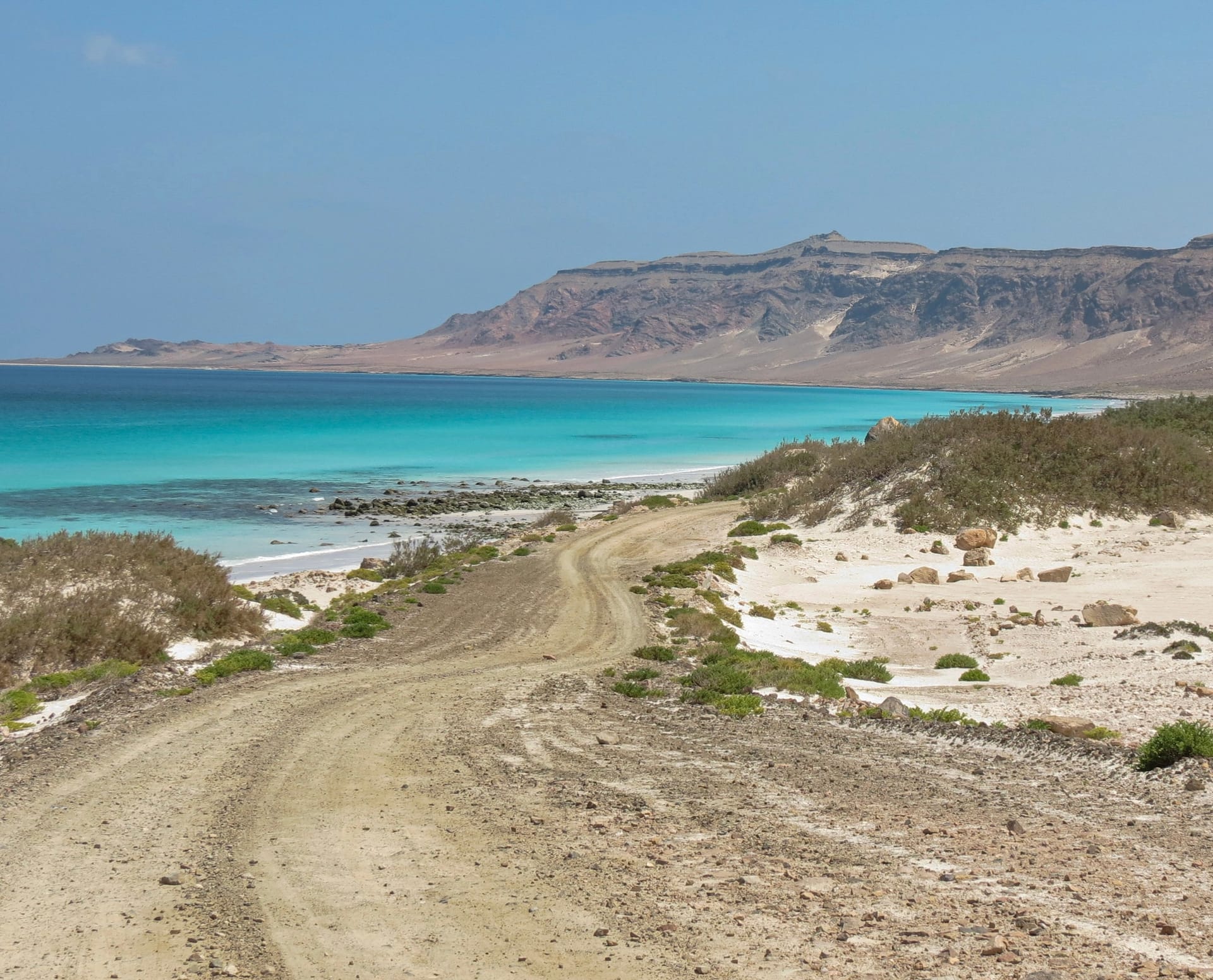 A sand track running down to a turquoise bay below a long escarpment on Socotra’s coast