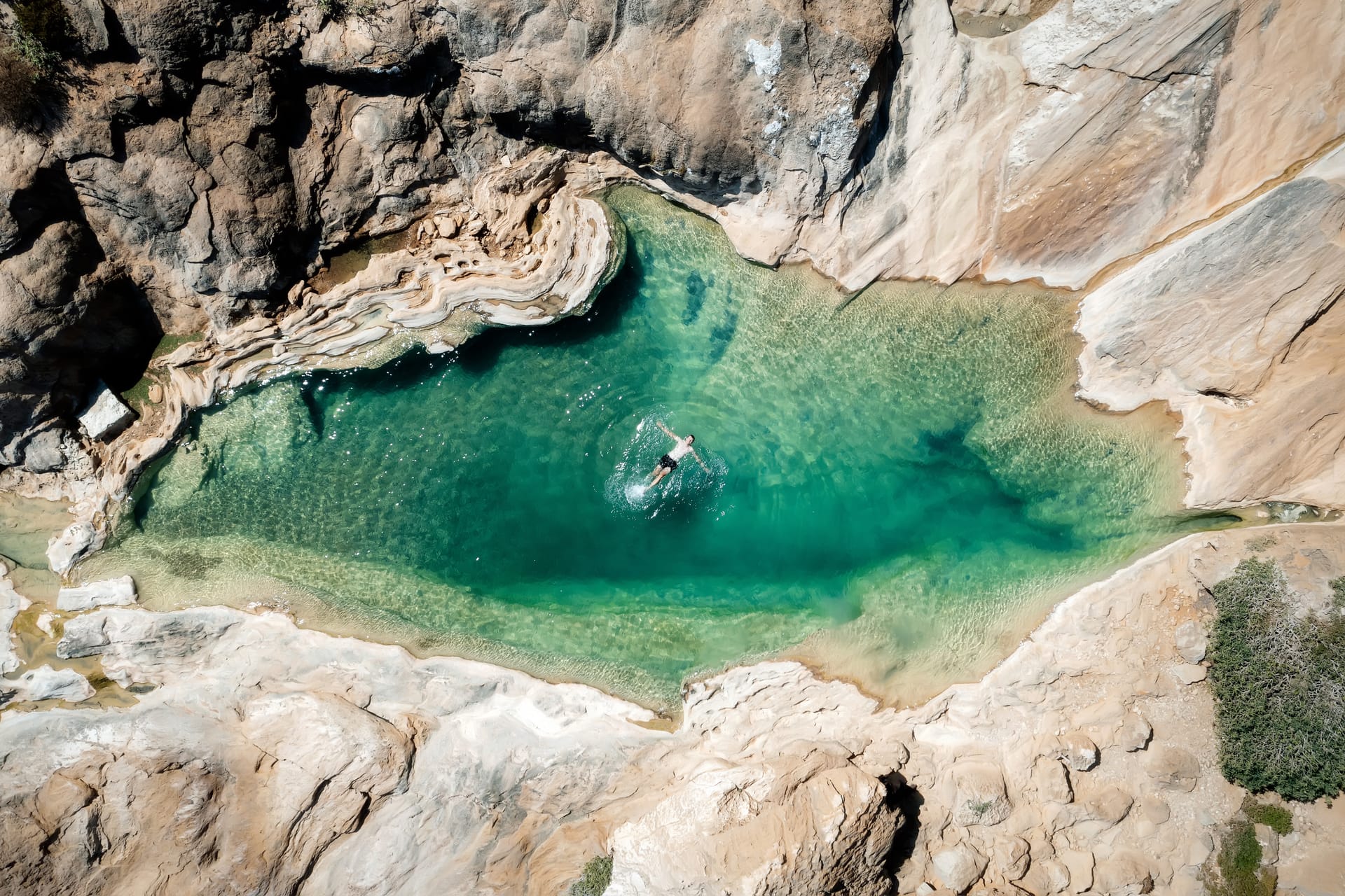 A swimmer in a green natural pool among pale limestone rocks, seen from above.